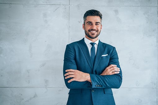 Portrait of handsome confident smiling businessman standing with arms crossed in the office and looking at camera.